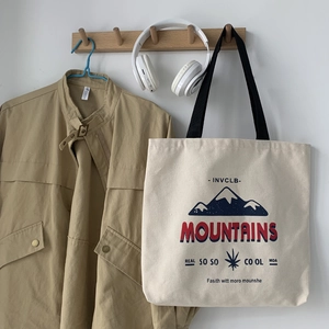 Close-up of beige canvas tote bag with mountain print hanging on a wooden hook