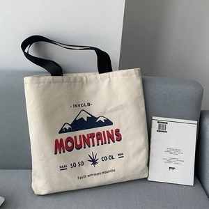 Detail of off-white canvas tote bag with mountain print and black straps on a sofa
