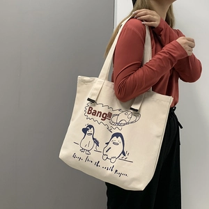 Close-up of a large beige canvas tote bag featuring cute cartoon penguin illustrations