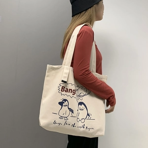 Side view of a large cream canvas tote bag with cartoon penguin print on a model