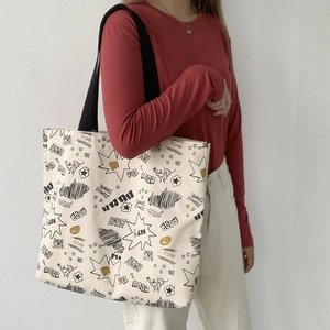 Detail view of large canvas tote bag with graffiti prints worn over a red shirt