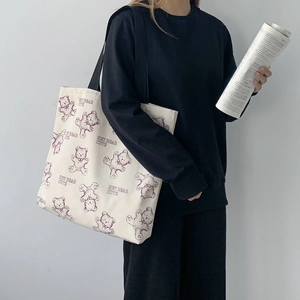 Detail of beige canvas tote bag featuring purple cartoon bear and black shoulder strap
