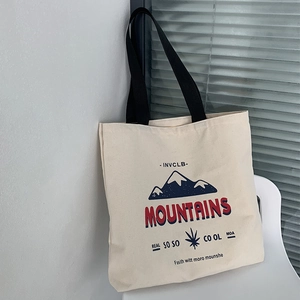 Detail of off-white canvas tote bag featuring mountain print and black handles