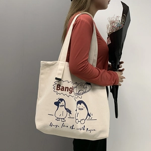 Detail of wide shoulder strap on cream canvas tote bag with blue cartoon penguin print