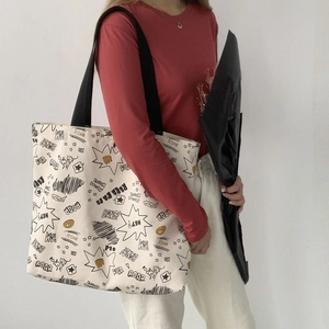 Detailed view of cream canvas tote bag featuring comic style graffiti and wide black strap