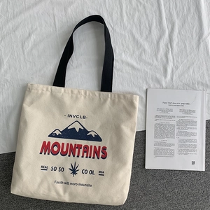 Minimalist beige canvas tote bag with mountain print and black straps on fabric