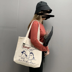 Off-white canvas tote bag with cartoon penguin print shown on a model for daily travel use