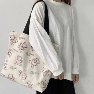 Detailed view of cream canvas tote bag with purple bear print and black strap on model
