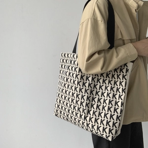 Dettaglio della borsa tote in tela con motivo K nero ripetuto su tessuto beige