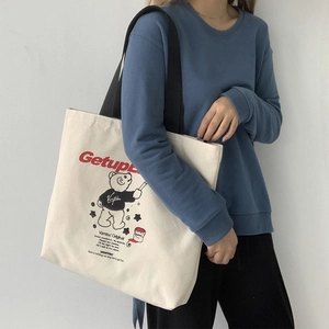 Detailed shot of an off-white canvas tote bag featuring a cute cartoon bear and black straps