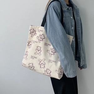 Close-up of off-white canvas tote bag featuring purple cartoon bear prints and black straps