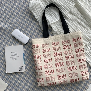 Flat lay of cream canvas tote bag with red Chinese fortune text and black wide straps