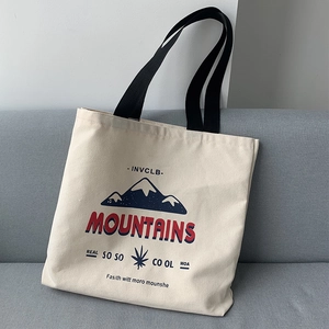 Detail of canvas tote bag showing mountain print and red MOUNTAINS text on beige fabric