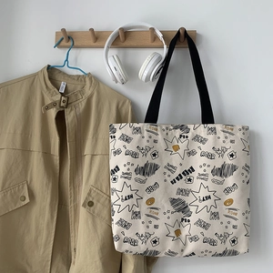 Close-up of beige canvas tote bag with comic graffiti patterns hanging on a wooden hook