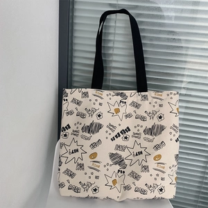 Detail of beige canvas tote bag featuring all-over comic book print and black straps