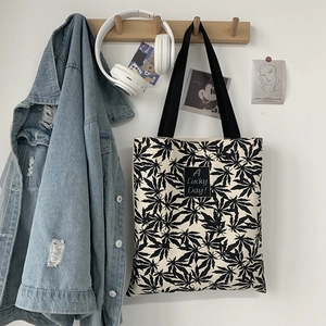 Détail du sac cabas en toile avec motif de feuilles et étiquette 'A Lucky Day!' sur mur