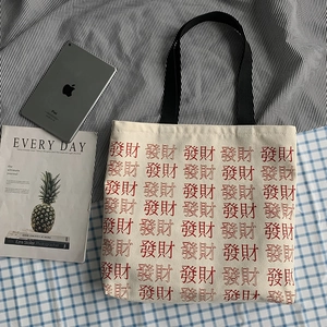 Flat lay of large canvas tote bag with red Chinese Fā Cái characters and black straps
