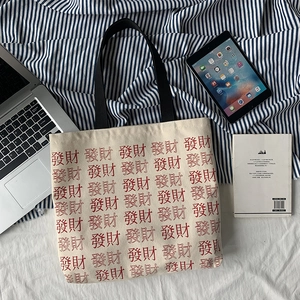 Overhead shot of a large beige canvas tote bag with red Chinese characters and laptop