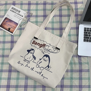 Flat lay of canvas tote bag with penguin cartoon and laptop on plaid fabric
