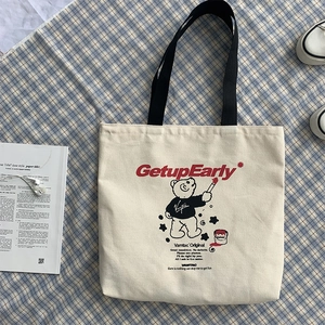 Close-up of cream canvas tote bag with red typography and bear graphic on plaid background