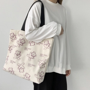 Detail of canvas tote bag featuring purple cartoon bear print and black shoulder straps