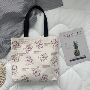 Close-up of a white canvas tote bag featuring a cute purple cartoon bear and strap