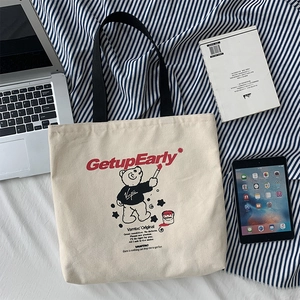 Detail of canvas tote bag featuring a red slogan and cute cartoon bear graphic