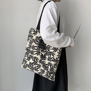 Détail du sac cabas en toile avec imprimé feuilles noires et étiquette 'A Lucky Day'