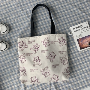 Detail view of off-white canvas tote bag with purple bear prints and black straps