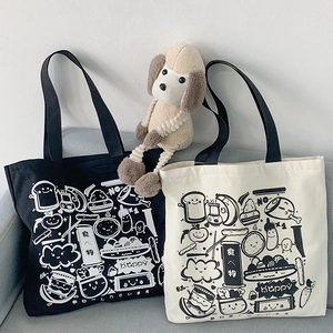 Canvas tote bags in black and cream featuring cute food doodle prints on a grey sofa