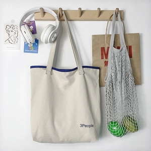 Borsa tote in tela con bordo blu e logo 3People appesa a un gancio in legno minimalista