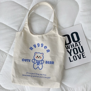 Dettaglio borsa tote in tela beige con orsetto blu su sfondo trapuntato morbido e pulito