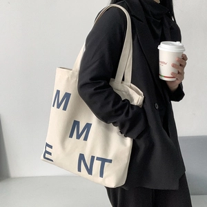 Detail of a large canvas tote bag with blue letter print worn over the shoulder