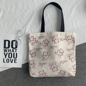 Detail of off-white canvas tote bag with purple bear pattern and black handles