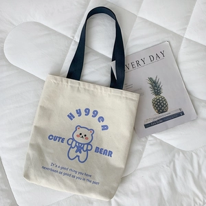 Dettaglio della borsa tote in tela con stampa orso blu e cinturino nero su base bianca
