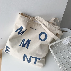 Detailed close-up of off-white canvas tote bag featuring navy blue MOMENT letter print