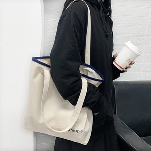 Dettaglio della borsa tote in tela bianco avorio con bordo blu e stampa di lettere