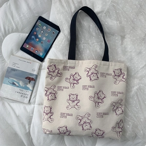 Detail view of beige canvas tote with purple cartoon bear and black webbing handles