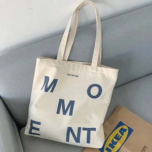 Minimalist canvas tote bag with MOMENT lettering shown on a grey fabric sofa