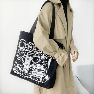 Detail of large black canvas tote bag with white hand-drawn cartoon illustrations on model