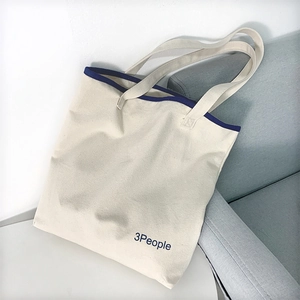 Dettaglio della borsa tote in tela crema con bordo blu e logo 3People sul divano