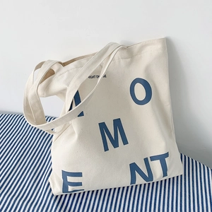 Detail of cream canvas tote bag featuring blue MOMENT lettering and minimalist texture