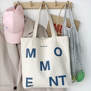 Detail of cream canvas tote bag with MOMENT lettering hanging on a wooden hook