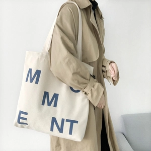 Close-up of a cream canvas tote bag featuring a blue M M E N T graphic and clear texture