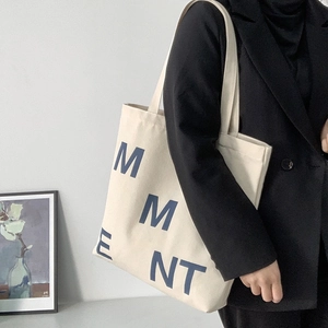 Minimalist canvas tote bag with bold blue lettering shown on a shoulder in a lifestyle setting