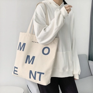Shoulder strap detail of a beige canvas tote bag with navy blue 'MOMENT' lettering