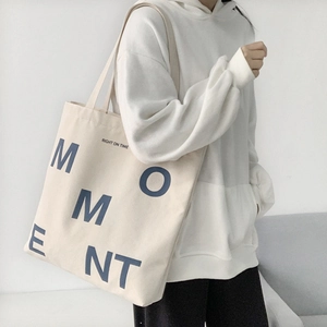 Detail of a cream canvas tote bag featuring blue letter print and large capacity design
