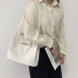 Detail of white nylon waterproof tote bag featuring a stitched brand logo label and long straps
