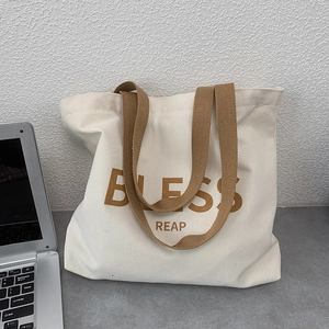Dettaglio di una borsa in tela spessa con tracolla intrecciata marrone e stampa BLESS