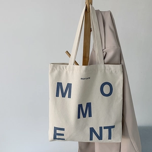 Detailed view of durable off-white canvas tote bag featuring navy blue MOMENT letter print